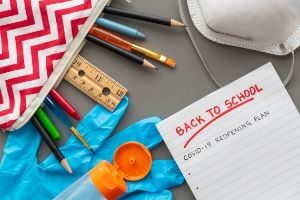 Picture of school supplies and pad that says back to school covid 19 plan