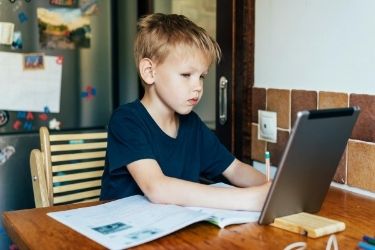 Young boy on tablet at kitchen table doing school work.